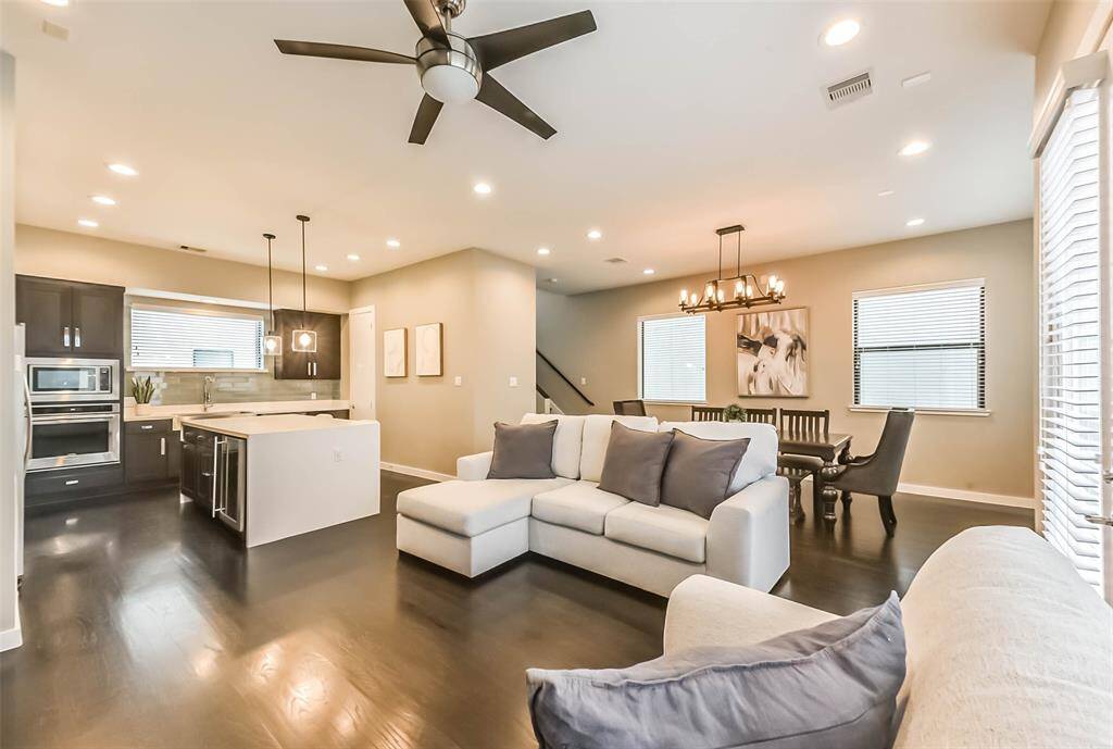 This open-concept living spacefeatures a stylish kitchen withdark cabinetry, quartzcountertops, a sleek island witha built-in wine fridge, andmodern pendant lighting. Thespacious living and dining areasboast elegant fixtures, recessedlighting, and large windows fornatural light. A neutral colorpalette, dark hardwood floors,and contemporary designelements create a sophisticatedyet cozy atmosphere, perfect forentertaining or relaxing.