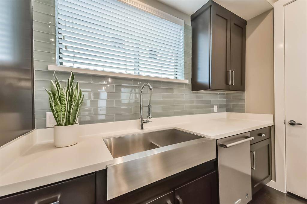 This modern kitchen featuressleek quartz countertops, richdark cabinetry, and a stylishsubway tile backsplash. A largewaterfall island offers ampleseating and workspace,complemented by chic pendantlighting. Stainless steelappliances, including a gascooktop and built-in microwave,add to the contemporary appeal.A deep farmhouse sink beneatha bright window enhancesfunctionality, while recessedlighting and an open layout makethis space perfect for cookingand entertaining.