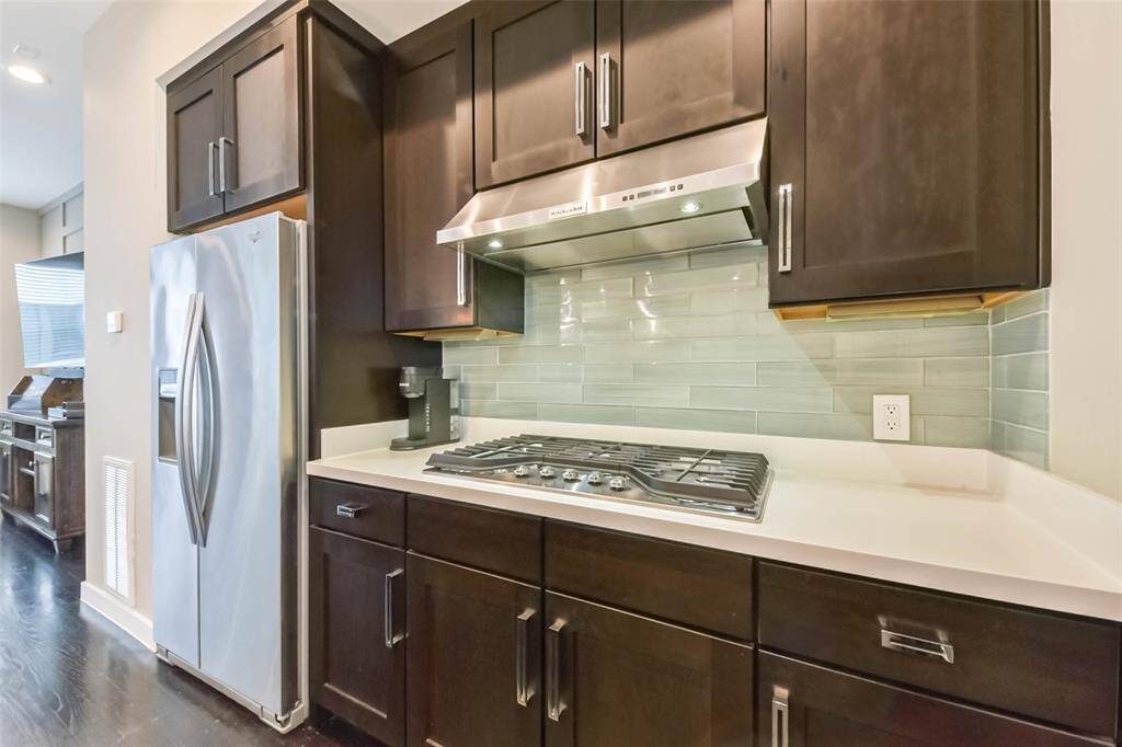 This modern kitchen featuressleek quartz countertops, richdark cabinetry, and a stylishsubway tile backsplash. A largewaterfall island offers ampleseating and workspace,complemented by chic pendantlighting. Stainless steelappliances, including a gascooktop and built-in microwave,add to the contemporary appeal.A deep farmhouse sink beneatha bright window enhancesfunctionality, while recessedlighting and an open layout makethis space perfect for cookingand entertaining.