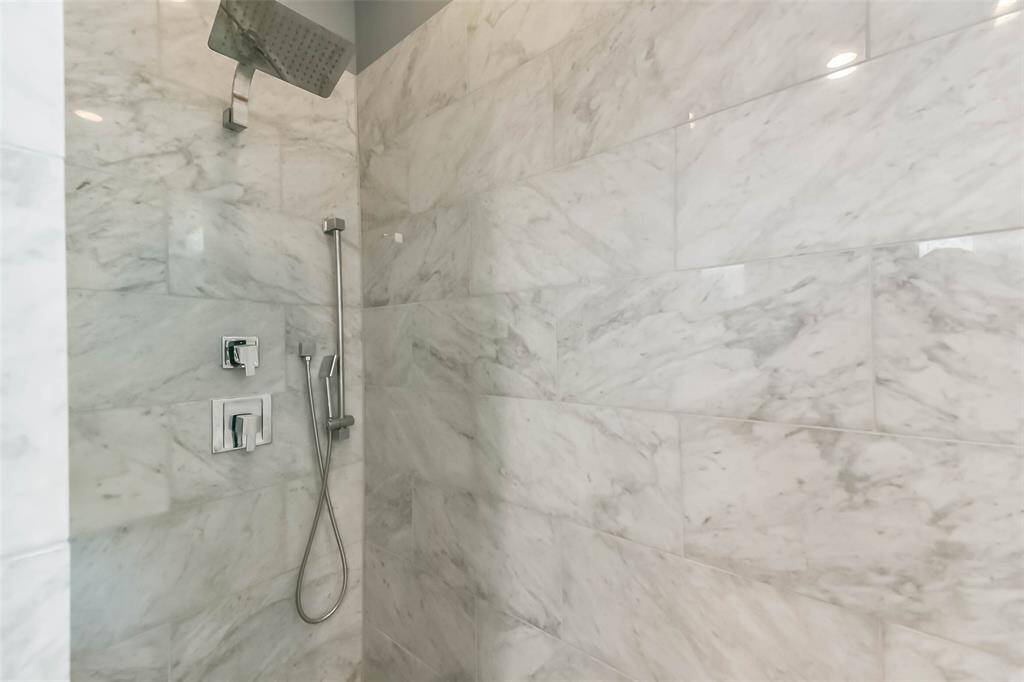 This luxurious master bathroomfeatures a sleek double vanitywith marble countertops, a largeframed mirror, and modernfixtures. The spa-like walk-inshower is enclosed in glass andadorned with elegant marble tile.Soft gray walls complement theclean white finishes, creating asophisticated and tranquilretreat. Thoughtful design andhigh-end details make this spaceboth functional and stylish.