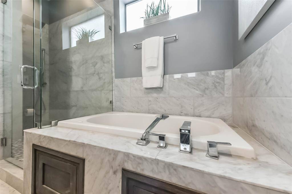 This luxurious master bathroomfeatures a sleek double vanitywith marble countertops, a largeframed mirror, and modernfixtures. The spa-like walk-inshower is enclosed in glass andadorned with elegant marble tile.Soft gray walls complement theclean white finishes, creating asophisticated and tranquilretreat. Thoughtful design andhigh-end details make this spaceboth functional and stylish.