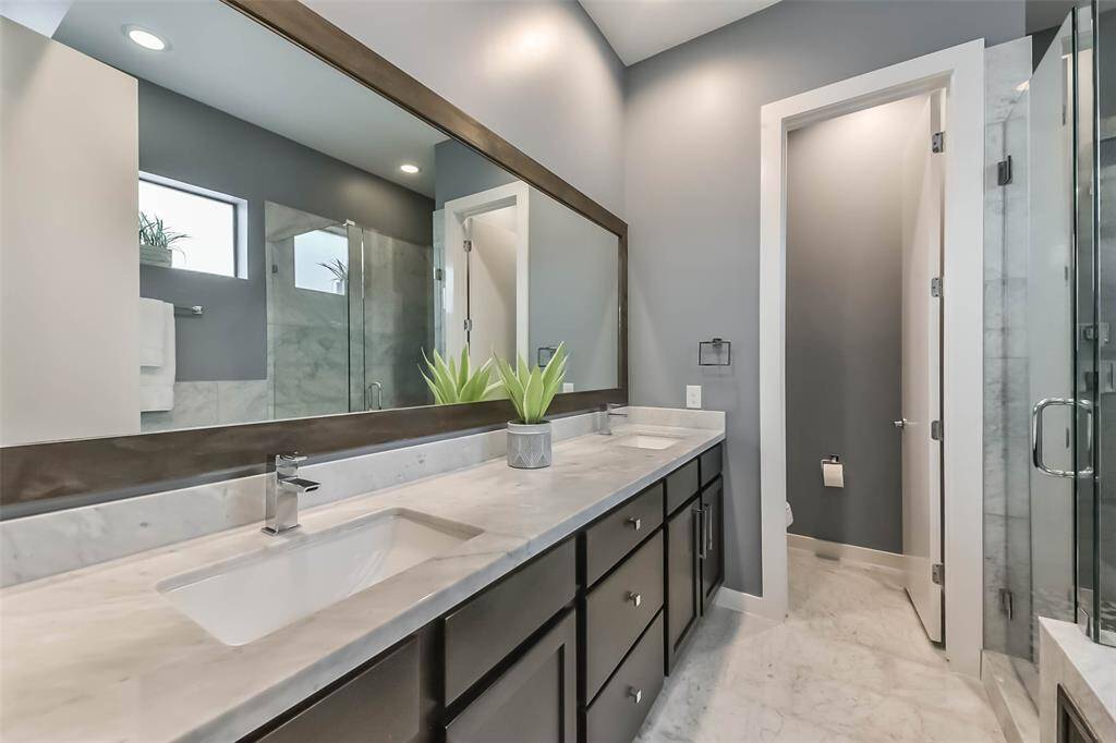 This luxurious master bathroomfeatures a sleek double vanitywith marble countertops, a largeframed mirror, and modernfixtures. The spa-like walk-inshower is enclosed in glass andadorned with elegant marble tile.Soft gray walls complement theclean white finishes, creating asophisticated and tranquilretreat. Thoughtful design andhigh-end details make this spaceboth functional and stylish.