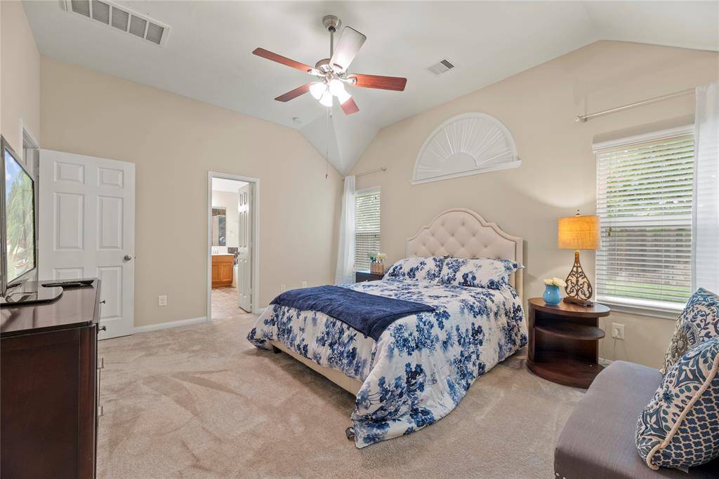 Spacious primary bedroom offers plush carpet, ceiling fan, high ceiling, walk-in closet and an en-suite bathroom.