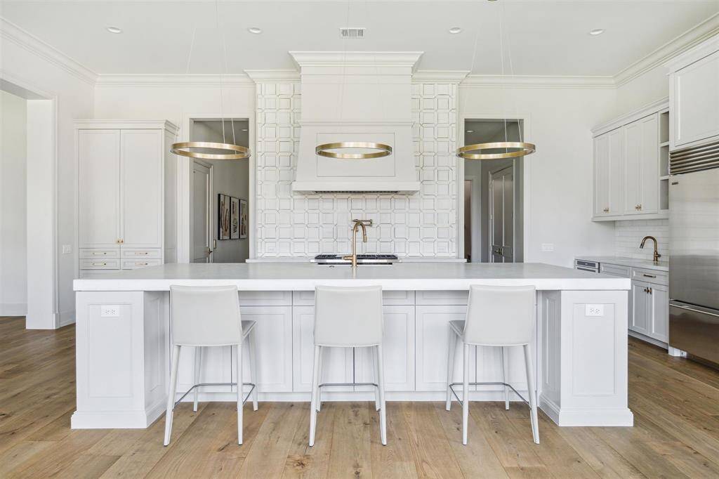 This stunning kitchen features a one-of-a-kind island with a spacious breakfast bar, offering seating for four. Topped with exquisite Opal White marble, the island is complemented by a sleek Blanco Specialty sink and a luxe gold Brizo faucet. Overhead, designer pendant lighting adds a touch of sophistication, enhancing the kitchen’s elegant and functional design.