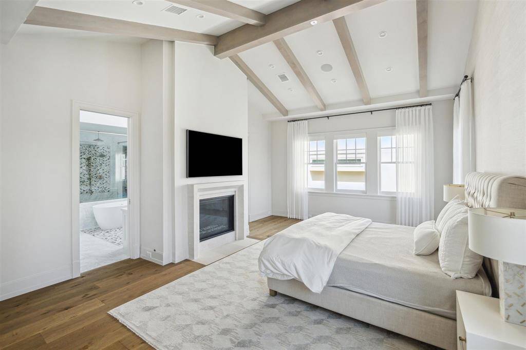 The breathtaking primary bedroom is a private retreat, exuding serenity and sophistication. Majestic white pine ceiling beams complement the abundant natural light. Expansive windows enhance the suite’s elegance, offering stunning green views that create a dreamy and tranquil ambiance.