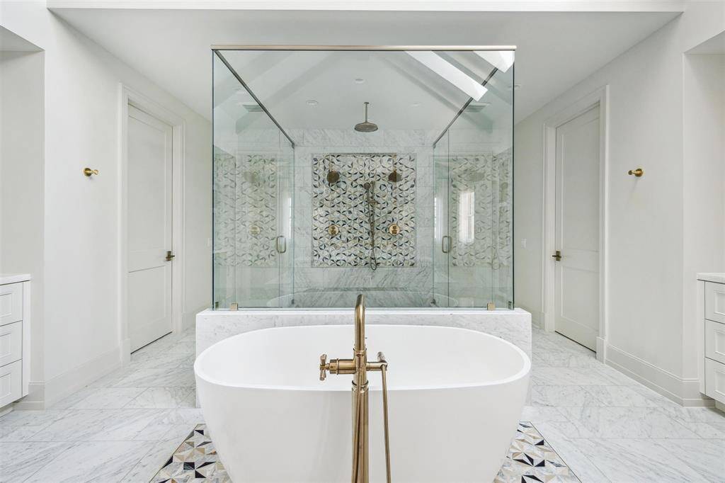 The stunning primary bath is a true sanctuary, featuring an oversized 7x7 glass-enclosed walk-in shower, a luxurious soaking tub, and elegant Carrara marble flooring. High ceilings with striking skylights fill the space with natural light, enhancing its spa-like ambiance.