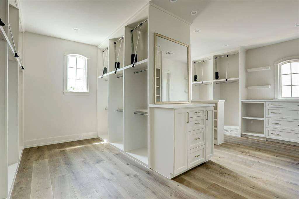 The expansive primary closet is a dream for any fashion enthusiast. Designed in a boutique style, it features abundant cabinetry and custom-built shelves for shoes and accessories. A spacious wall of hanging storage elegantly divides the room into two distinct closet spaces, offering both functionality and sophistication.