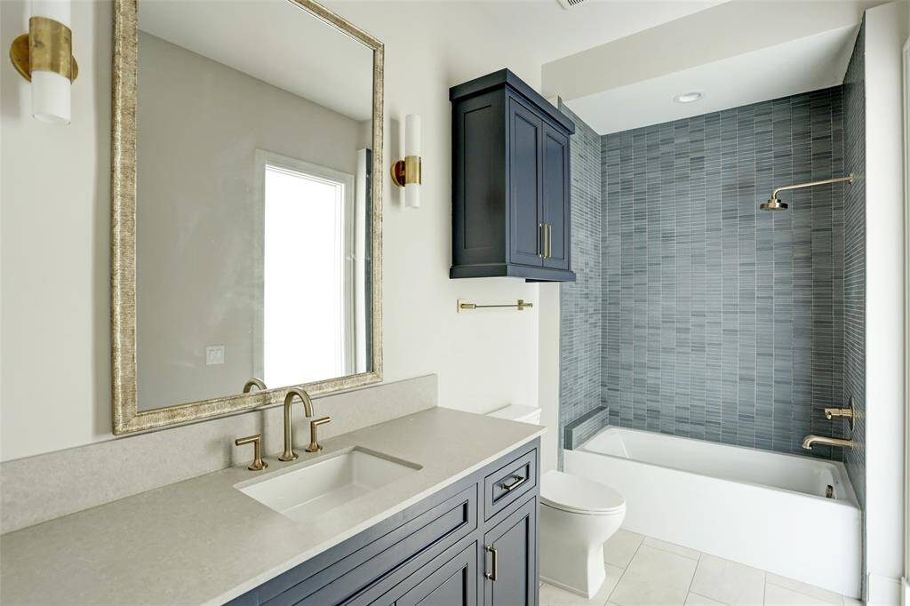 This stylish en-suite bath boasts a refined shower/tub combo adorned with mosaic stone tile, a sleek modern vanity with a rich wooden countertop, and an elegant framed mirror, blending sophistication with functionality.