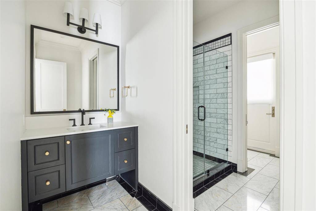 Blending luxury with practicality, this beautifully appointed first-floor en-suite features polished Carrara marble tile in a farmhouse stone pattern, sleek honed quartz countertops, custom cabinetry, and a generously sized glass-enclosed walk-in shower.