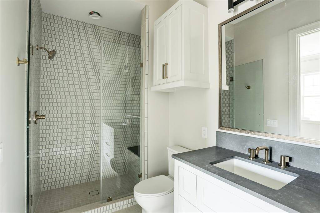 This beautifully designed en-suite showcases a glass-enclosed shower with a built-in bench and elegant mosaic stone surround. A sleek quartz vanity, custom cabinetry, and a designer mirror complete the space with timeless style and sophistication.
