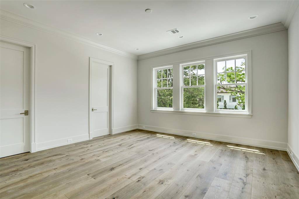 One of five generously sized secondary bedrooms, this light-filled space features soaring ceilings, expansive windows, a walk-in closet with built-in hanging storage, and elegant white oak hardwood floors.