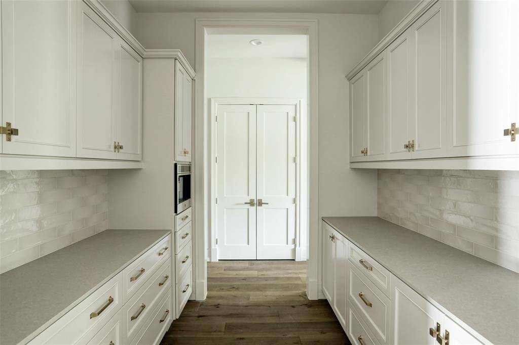 The thoughtfully designed pantry offers ample counter space and features a built-in JennAir coffee maker for ultimate convenience. Stylish custom wooden cabinetry, accented with designer hardware, adds a touch of sophistication, while honed quartz countertops seamlessly complement the space. Designed for both function and elegance, this pantry enhances effortless entertaining.