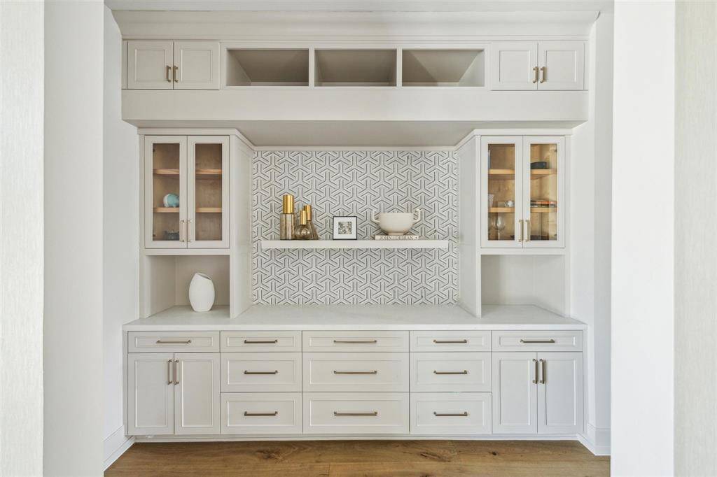 This beautifully designed butler’s pantry serves as a seamless transition between the kitchen and dining room. Topped with luxurious Opal White Satin Marble, the space is complemented by custom cabinetry, glass-front display shelves, and ample storage, combining both elegance and functionality for effortless entertaining.