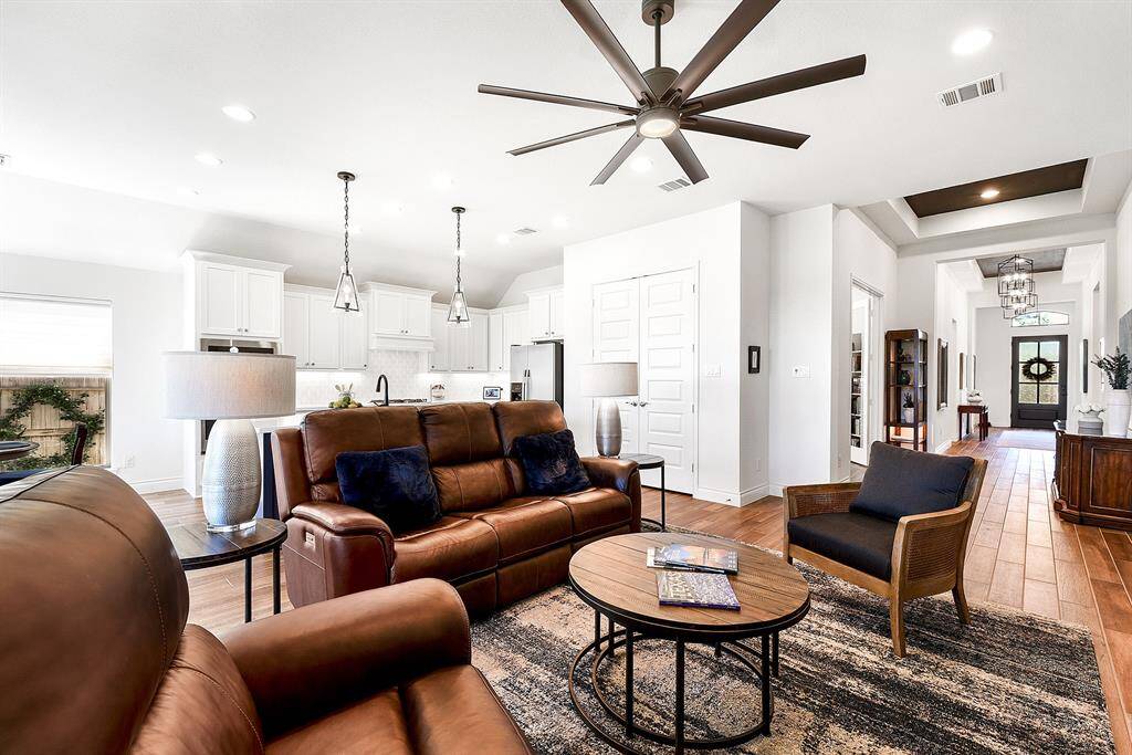 A grand view of the home showcases its spacious, open layout with high ceilings, an 8-blade drop-down ceiling fan, wood-like tiled floors, recessed lighting, pendant lighting, and more.