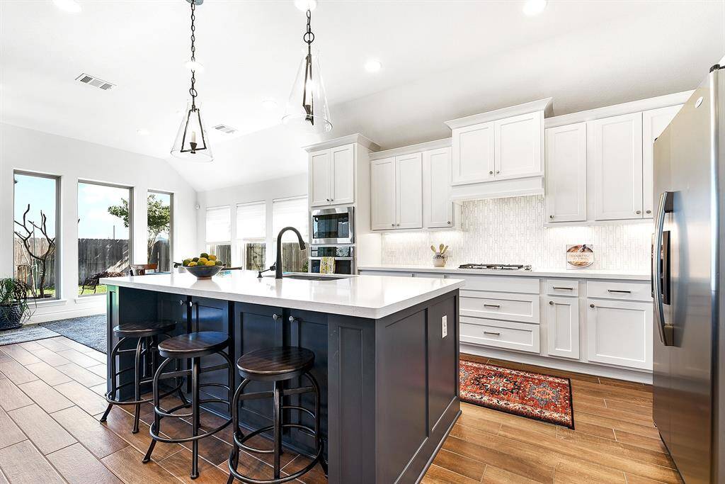 he large island features navy blue accents, with a farmhouse sink that faces out toward the living room. It also includes a spacious breakfast bar with plenty of seating and additional storage cabinets.