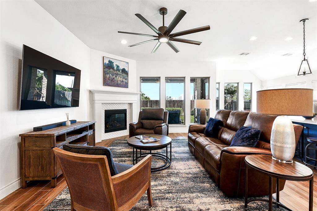 The living room features a gas fireplace, high ceilings, a drop-down ceiling fan, floor-to-ceiling windows, and wood-like flooring. The gas fireplace serves as the focal point of the room, offering a cozy atmosphere. There is plenty of space to accommodate any style of living room furniture you may have.