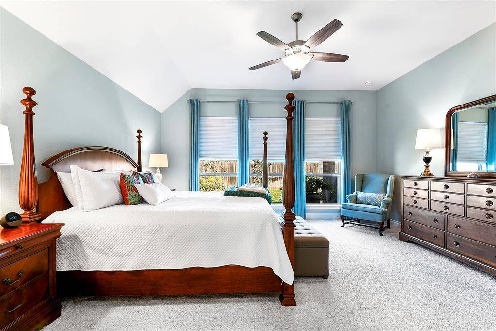 The large primary bedroom features high ceilings, a large ceiling fan, and custom window treatments, all with a beautiful view of the backyard. The bedroom is the only room with plush carpeting for added comfort.