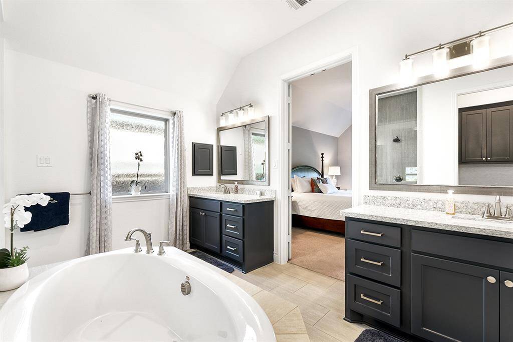 The large primary ensuite bathroom is spacious, featuring a separate garden tub, an oversized walk-in glass and tiled shower, and double vanity sinks with plenty of storage space.