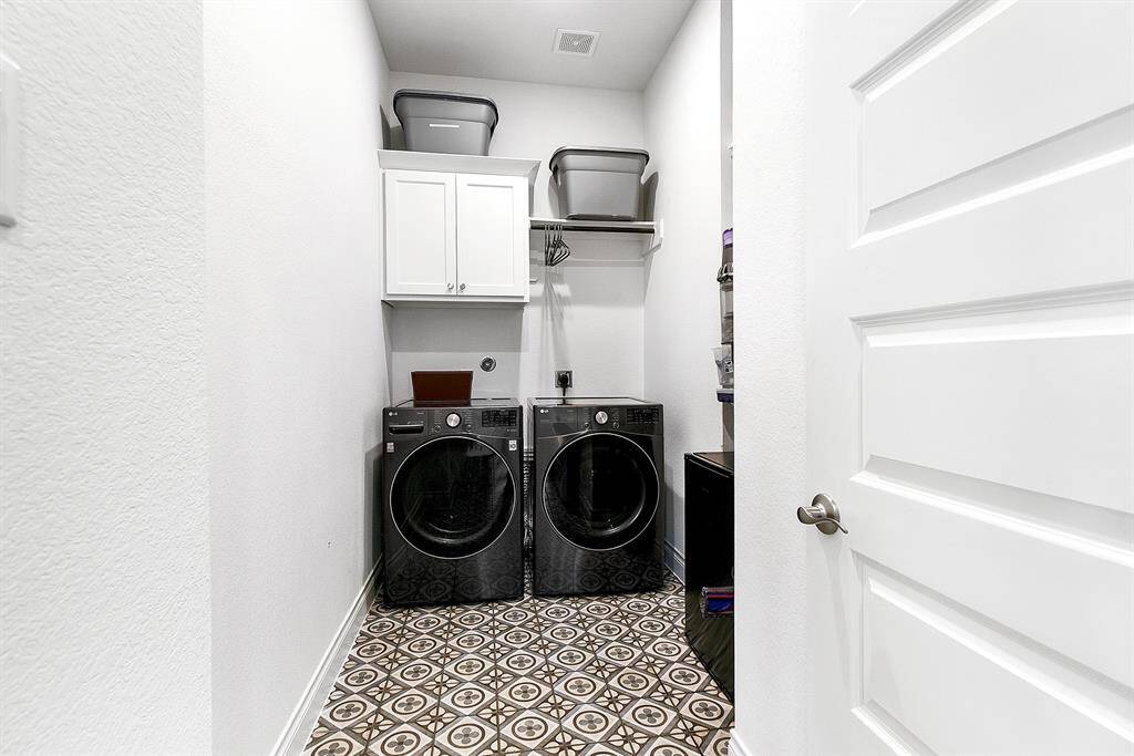 The utility room features built-in shelving, cabinetry, and a hanging rod, offering extra space for a second refrigerator or freezer. Notice the upgraded French-style tile that adds a stylish touch to the space.