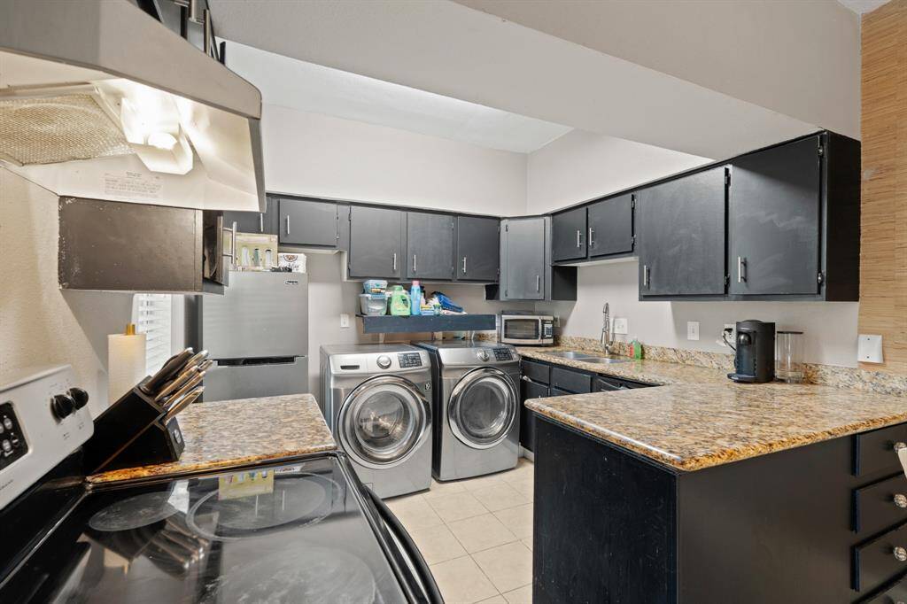 The kitchen features an included Samsung front-loading washer and dryer, neatly installed side by side with convenient shelving above for added storage. A spacious stainless steel refrigerator, also included, enhances the functionality of the space.