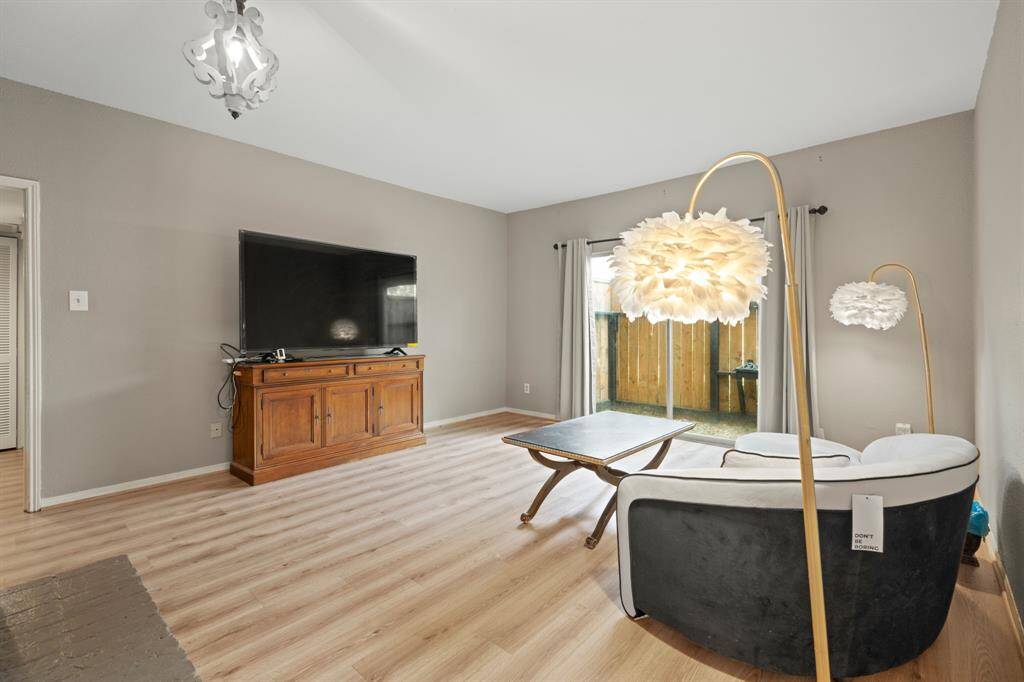 The spacious living room is bright and inviting, with natural light streaming through the sliding glass door and a modern chandelier adding a refined touch. The open layout enhances both comfort and versatility, offering an ideal setting for various activities.