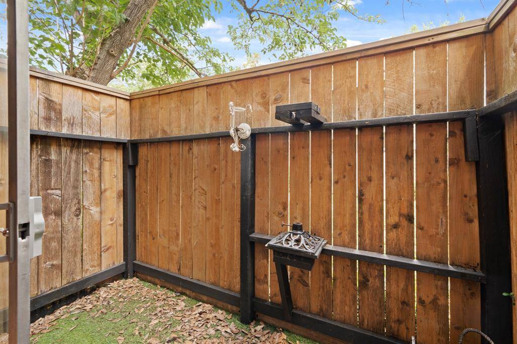 This charming enclosed patio offers a cozy outdoor retreat, framed by sturdy wooden fencing with sleek metal accents for added support and style. The artificial grass brings a touch of greenery and low-maintenance charm, while the trees and foliage lining the top of the fence provide privacy and a natural ambiance.