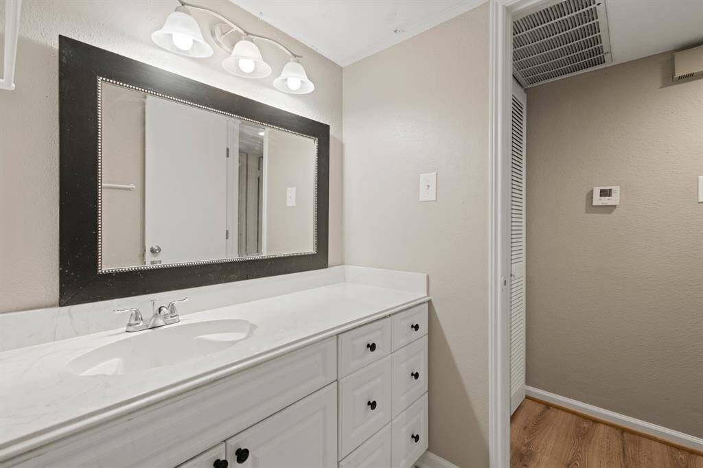 The primary bathroom features a spacious countertop with ample room for daily essentials, contributing to a serene and cohesive ambiance. A three-light fixture above the large mirror provides soft illumination, enhancing both style and functionality.