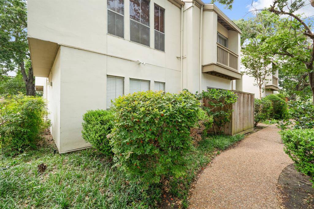 The walkway to the unit offers a clear and well-maintained path leading to the condo unit, surrounded by lush greenery and tall trees that create a serene and inviting approach. From this vantage point, the unit is located further down on the left, marked with a distinctive exterior and numbered for easy identification.