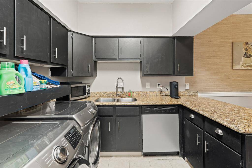 The kitchen features a stainless steel double-basin sink with a modern, curved faucet, complemented by a sleek stainless steel dishwasher directly below for added convenience. A microwave, which will stay with the unit, enhances functionality, creating a well-equipped space for daily tasks.