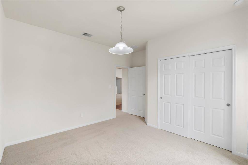 This room features neutral carpet and walls, a ceiling light fixture, and a double-door closet. It offers a clean and simple space, ideal for customization.