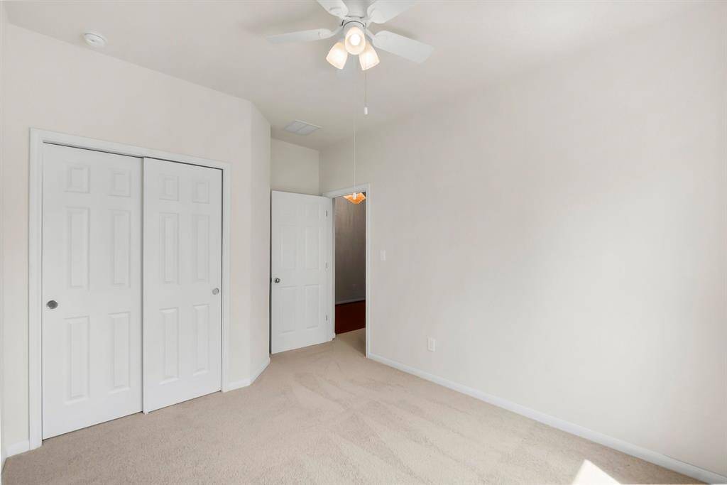 This room features neutral walls, a ceiling fan, carpeted flooring, and ample natural light. It includes a closet with double doors and an adjacent hallway entrance.