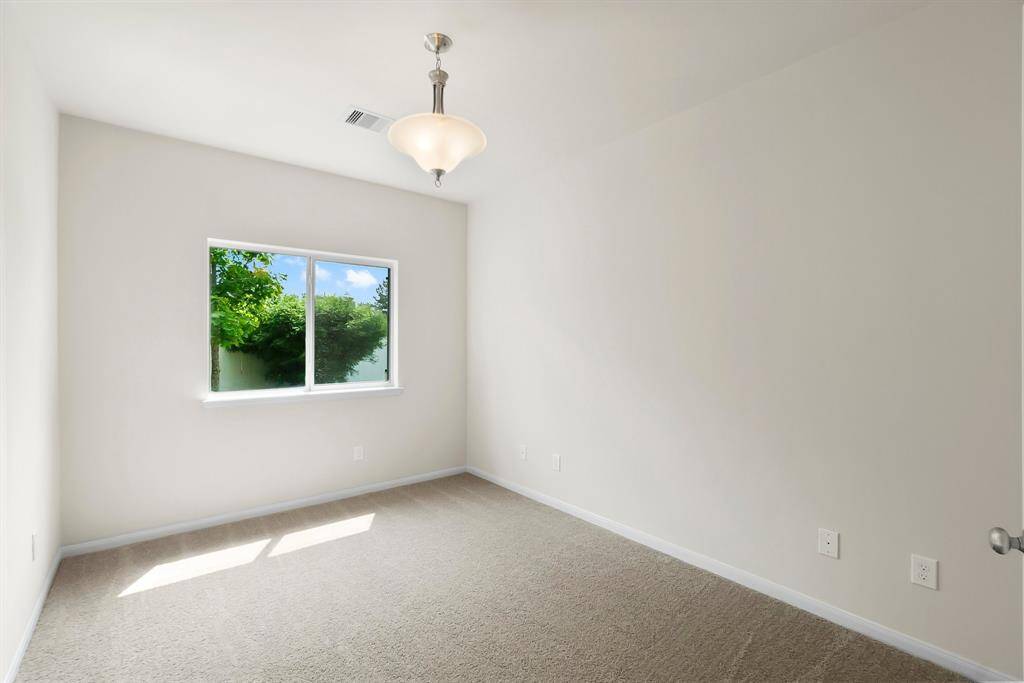 Bright, neutral room with a large window offering garden views, carpeted floor, and a modern light fixture. Perfect for a bedroom or office space.