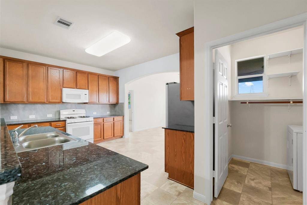 Bright, open kitchen with ample natural light, featuring wood cabinets, granite countertops, and modern appliances. The space flows into a living area, creating an inviting and functional layout.