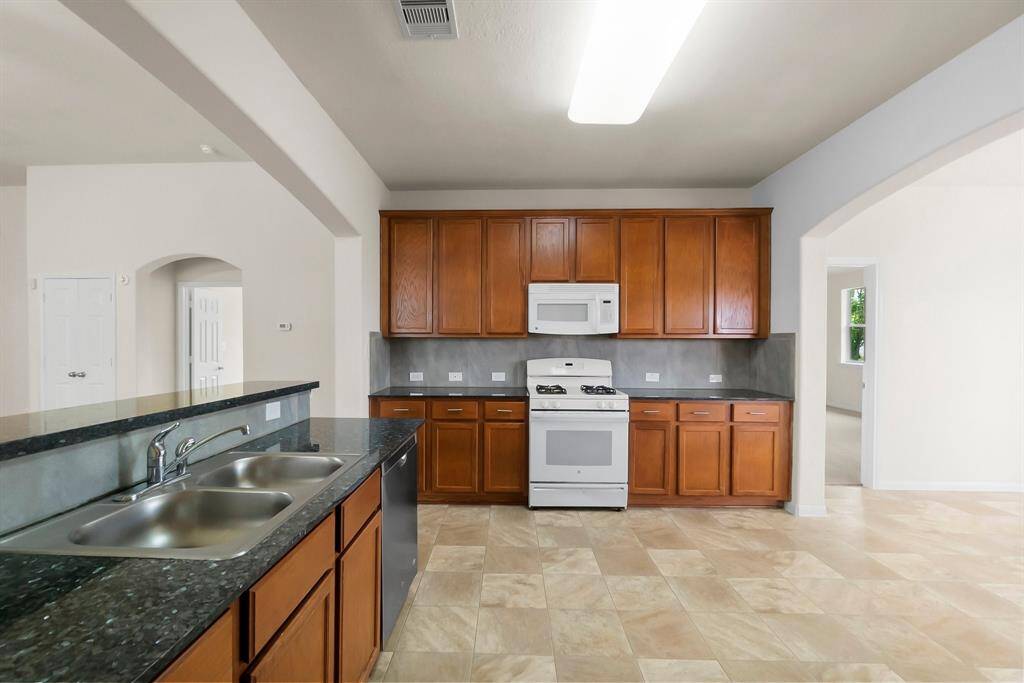 This photo showcases an open-concept kitchen and living area featuring a modern kitchen island with granite countertops, stainless steel appliances, and ample cabinetry. The kitchen flows into a spacious living room with large windows, neutral walls, and a ceiling fan, creating a bright and inviting atmosphere.