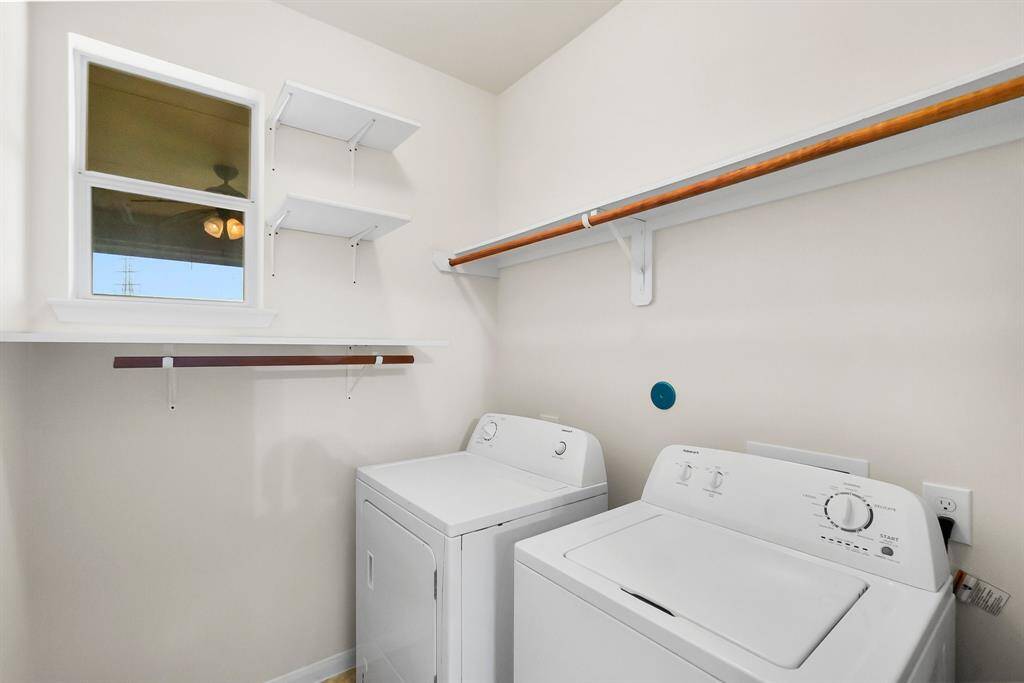 Modern kitchen with granite countertops, wooden cabinets, and a gas stove. Adjacent is a utility room with shelves and a window, offering additional storage and functionality. The space is bright and open, with a neutral color palette.
