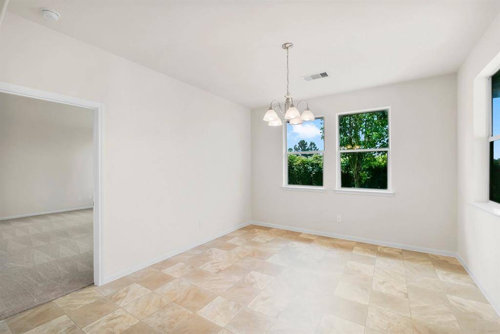 This kitchen features an open layout with ample natural light, a spacious central island with a double sink, elegant dark countertops, and warm wooden cabinetry. The room includes a white gas stove and microwave, offering a blend of functionality and style.