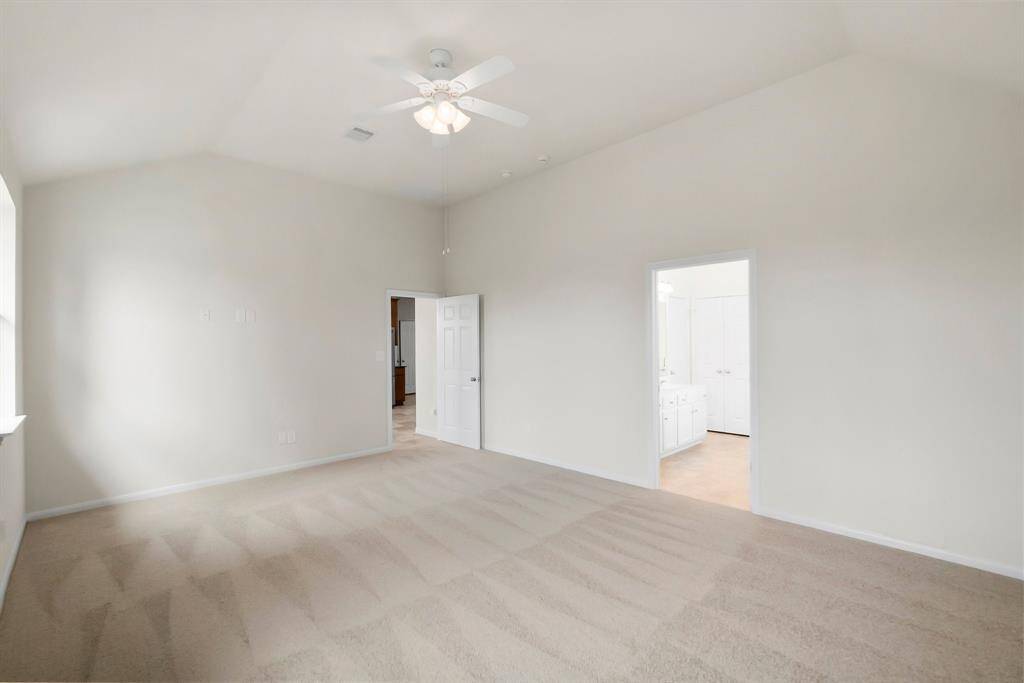 This photo shows a bright, open-concept dining and kitchen area with tiled flooring. The kitchen features modern appliances, including a stainless steel refrigerator and dishwasher, with a view to a fenced backyard through a window and door. A light fixture hangs above the dining space, and there's access to a living area through an arched opening.