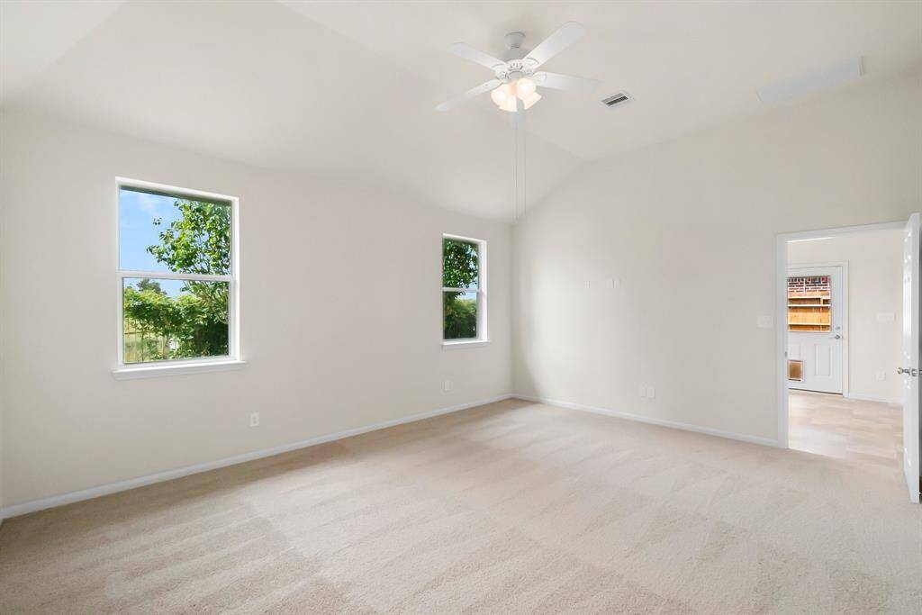 This spacious Primary,bedroom features neutral carpet, two windows with garden views, and a ceiling fan, perfect for a comfortable and airy living space.