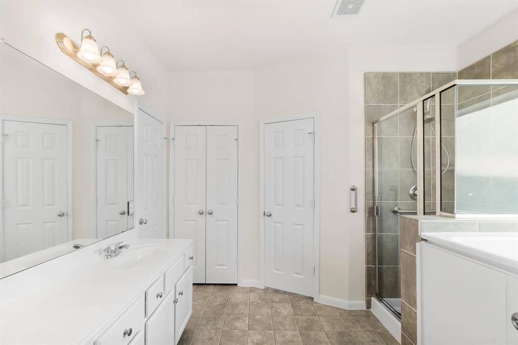 Bright and spacious bedroom with neutral walls, plush carpet, and two large windows offering plenty of natural light. The ceiling fan adds comfort, and the room connects to a tiled space through an open doorway.