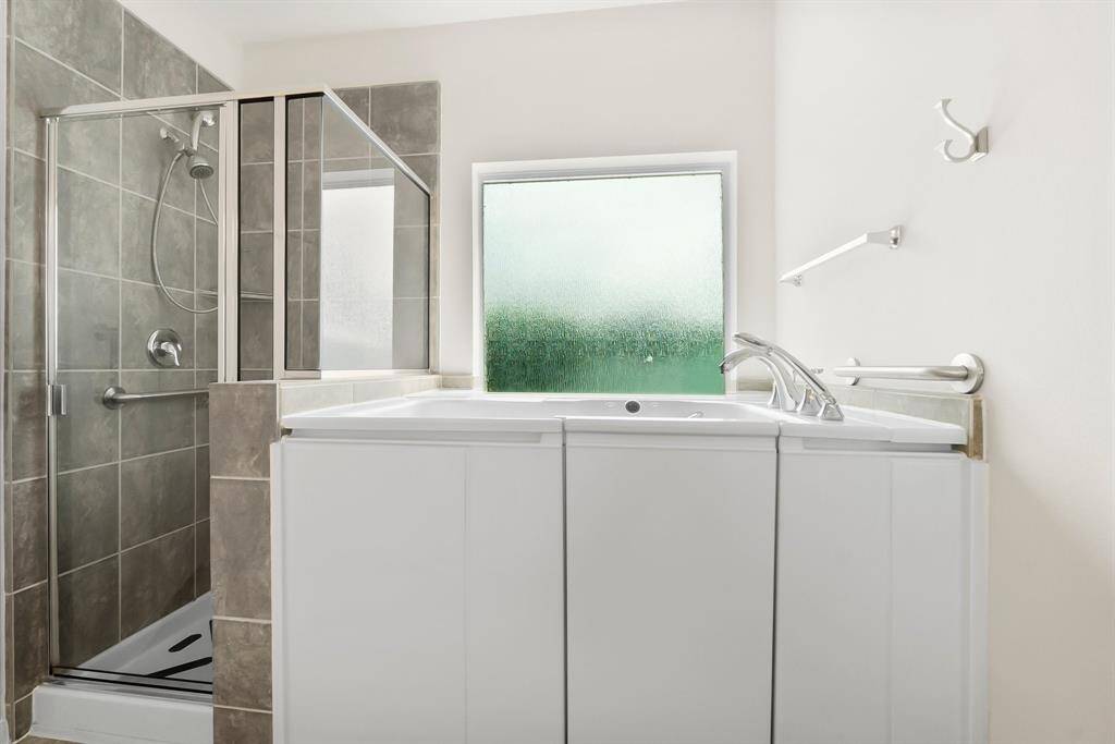 This bathroom features a double vanity with ample storage, large mirrors, and modern lighting. It includes a separate walk-in shower with neutral tile, and two white doors, offering a clean and bright space.