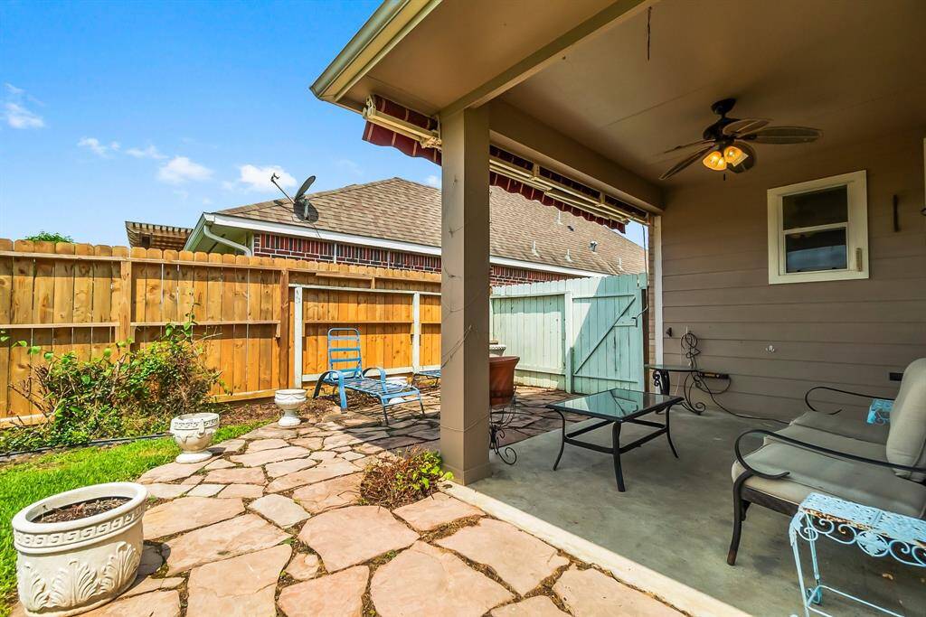 Cozy backyard patio with a ceiling fan and comfortable seating. The area features a mix of stone and grass, surrounded by a wooden fence, offering a private and inviting outdoor space.