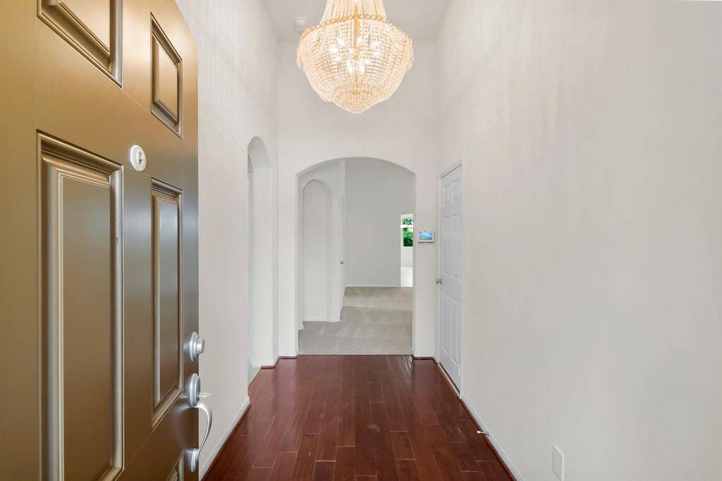 This entryway features a classic wooden door opening into a bright hallway with hardwood flooring. An elegant chandelier adds a touch of luxury, while arched openings lead to other rooms, creating a welcoming and sophisticated first impression.