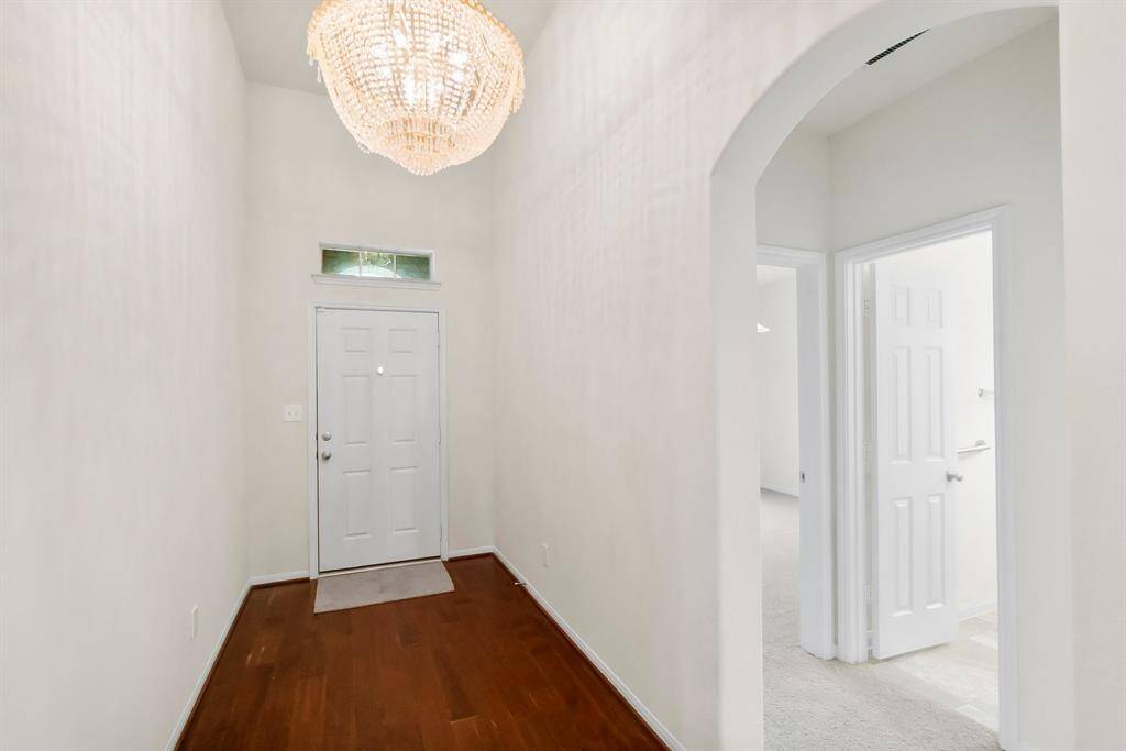 This entryway features a high ceiling and elegant chandelier, with hardwood flooring and an arched doorway leading to adjacent rooms.