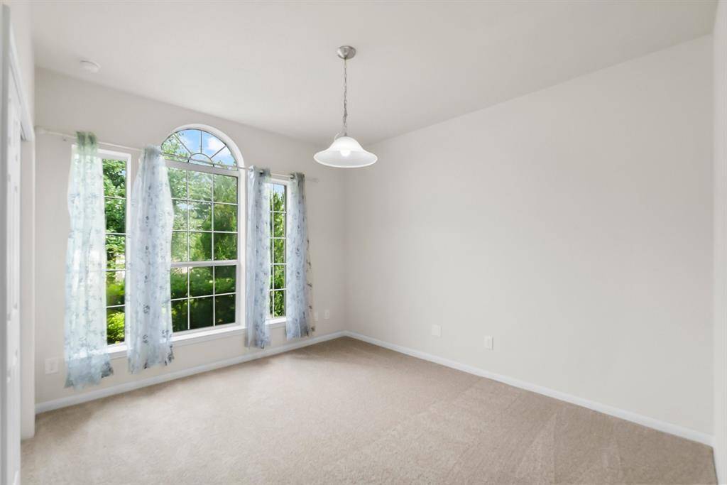 This bright room features a large, arched window with sheer curtains, neutral carpeting, and a pendant light fixture, offering a cozy and inviting atmosphere.