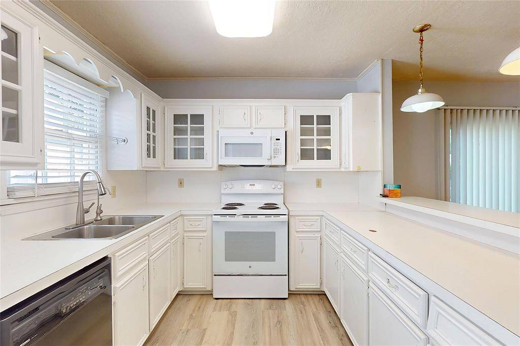 Bright, airy kitchen featuring white cabinetry, modern appliances, and new laminate flooring. Ample counter space and a double sink enhance functionality, while a pass-through window and pendant lighting add charm.