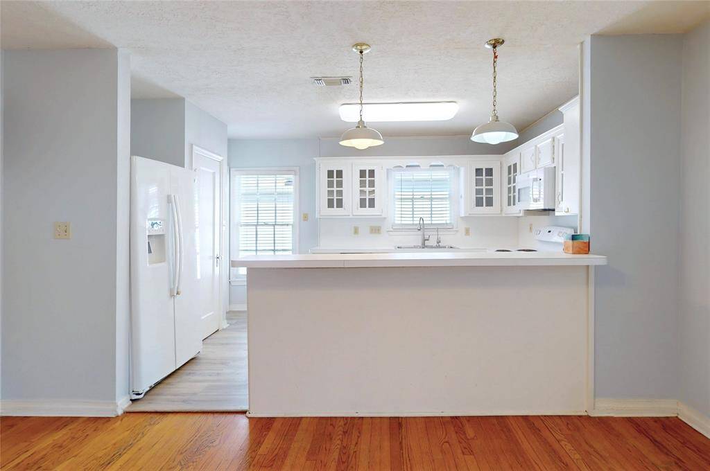 Bright and inviting kitchen with white cabinetry, a central island, and pendant lighting. It features a large window for natural light and hardwood flooring, creating a warm, open atmosphere.