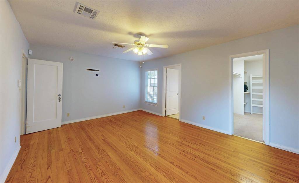 Another view of the primary bedroom with ample natural light.  Note the walk-in closet with built-in shelving. The neutral wall color provides a versatile backdrop.
