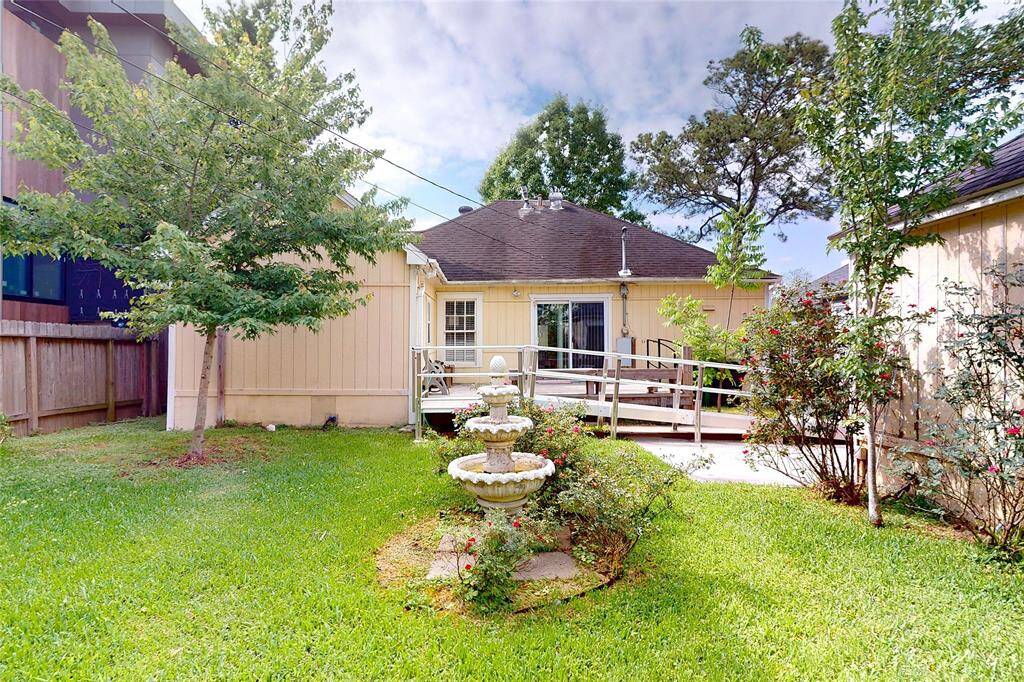Charming backyard with a well-maintained lawn, mature trees, and a decorative fountain. The house features a ramp leading to a cozy back entrance, ideal for accessibility. Perfect for outdoor relaxation and entertaining.