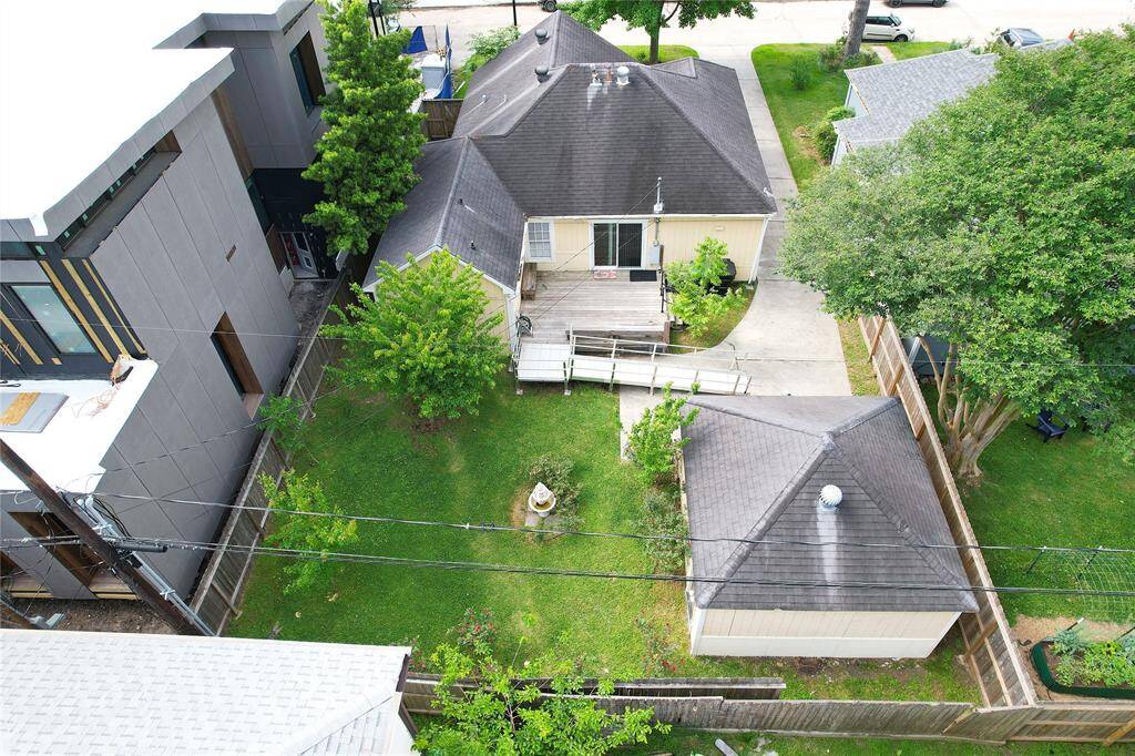 A cozy single family home nestled between modern structures. It features a spacious, well-maintained backyard with lush greenery and a detached garage. The property is fenced for privacy and has a small deck with a ramp leading to the back door.