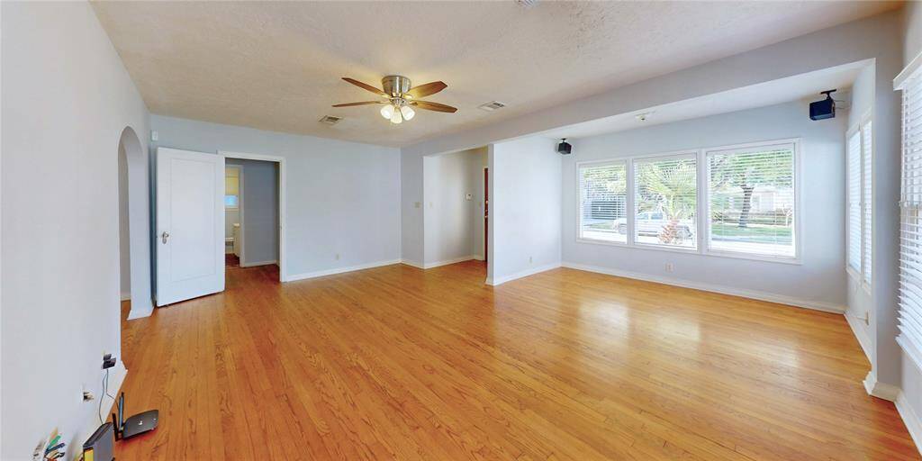 Living room features hardwood floors, large windows for natural light, a ceiling fan, and a neutral color palette. An arched doorway adds character, while an open layout provides versatility.
